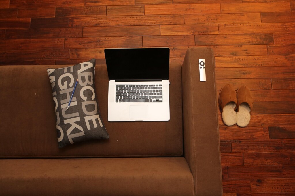 Overhead view of a home office scene with a couch, computer, slippers, and hardwood floor.