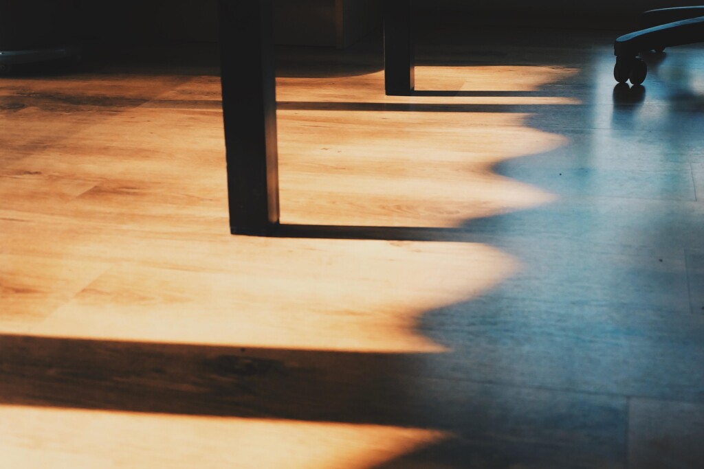 Hardwood floor illuminated by natural sunlight with shadows creating texture and depth.